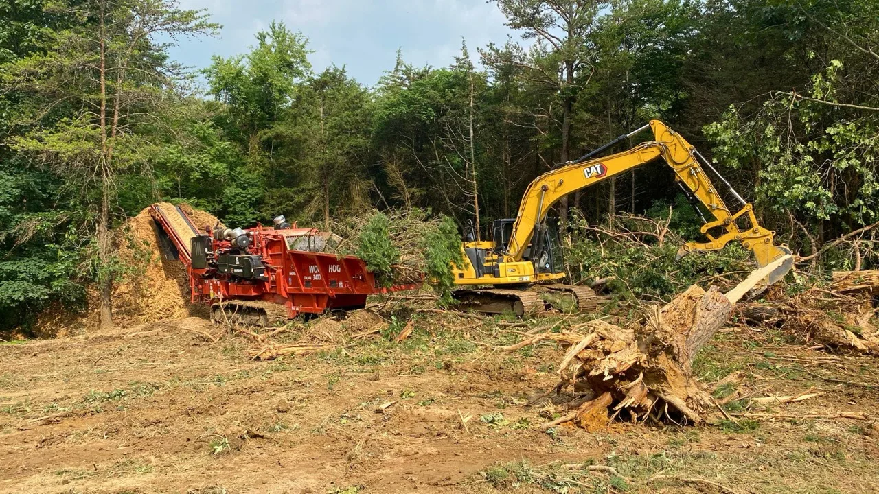 Excavator and wood chipper clearing a wooded lot the traditional way, with a large tree stump on the cleared ground