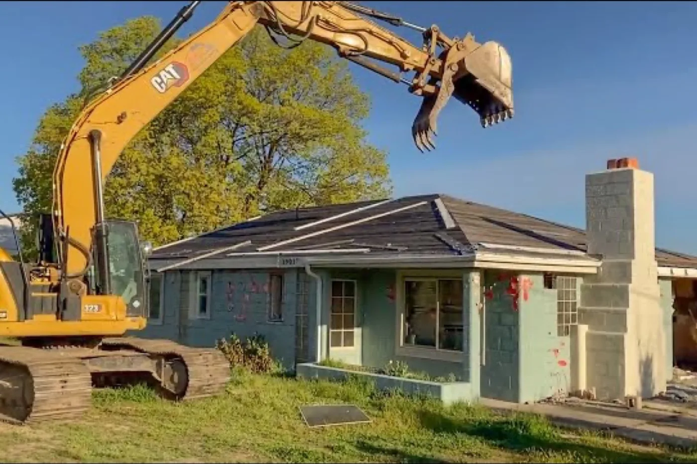 Excavator tearing down the roof of a small one-story house