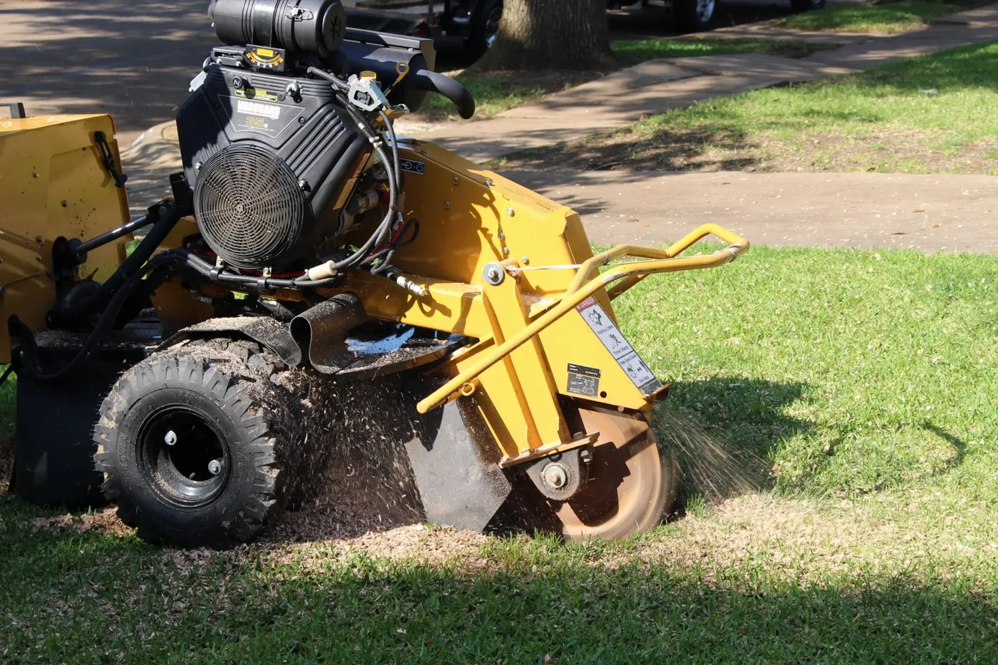 Yellow stump grinder cutting wheel grinding a stump in a grass lawn