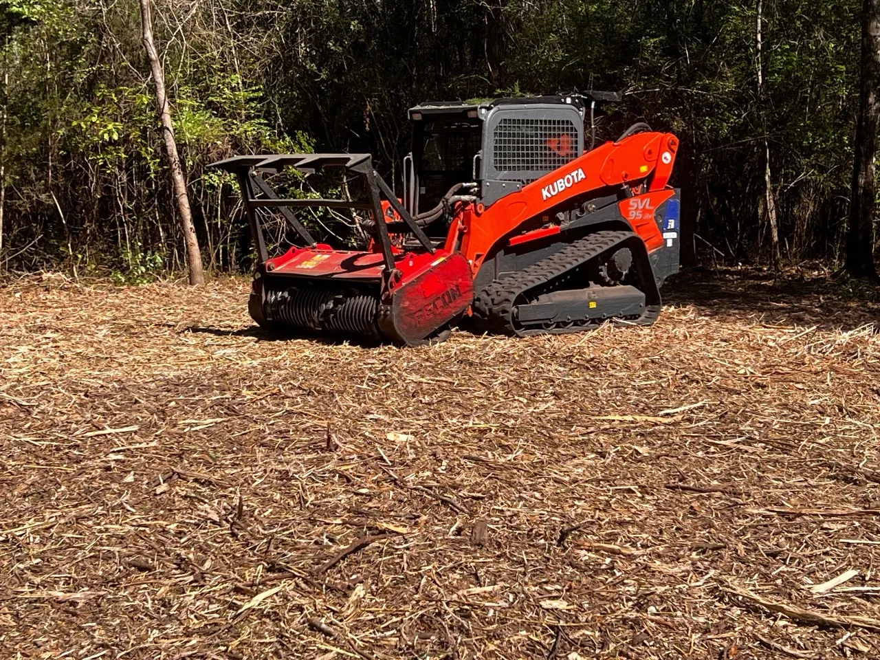 Compact track loader with a forestry mulching head on freshly mulched ground in the East Texas pines